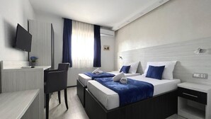 Habitación de hotel con dos camas, un escritorio, una silla, un televisor y una ventana con cortinas.