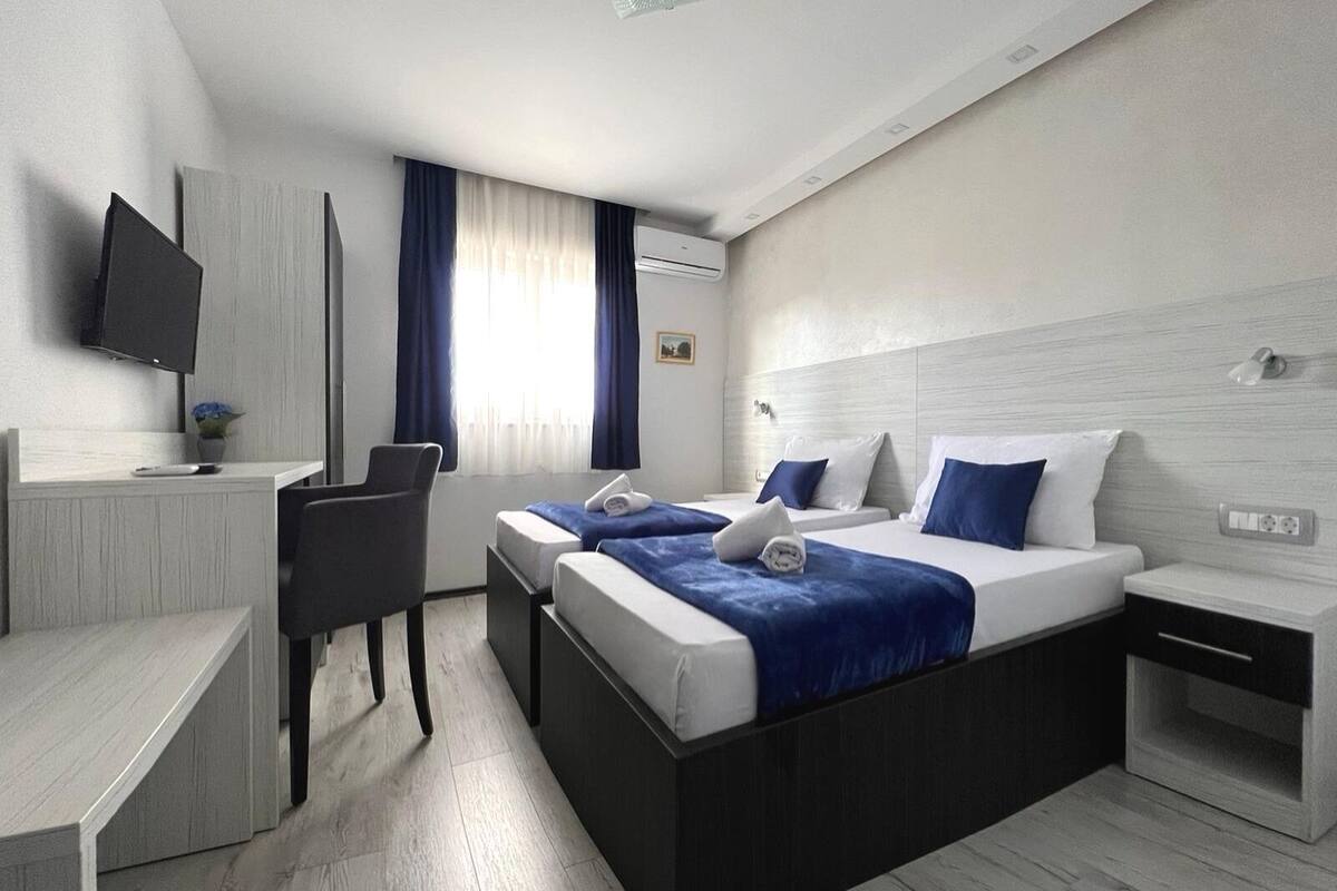 Une chambre d’hôtel avec deux lits, un bureau, une chaise, une télévision et une fenêtre avec des rideaux.