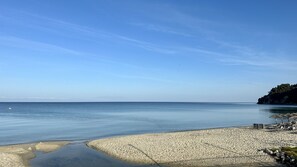Ein Strand mit klarem Himmel, ruhiger See und einem Felsenvorsprung.