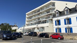 Ein mehrstöckiges Gebäude mit Balkonen, ein Parkplatz mit verschiedenen Autos und eine Fußgängerüberweg.