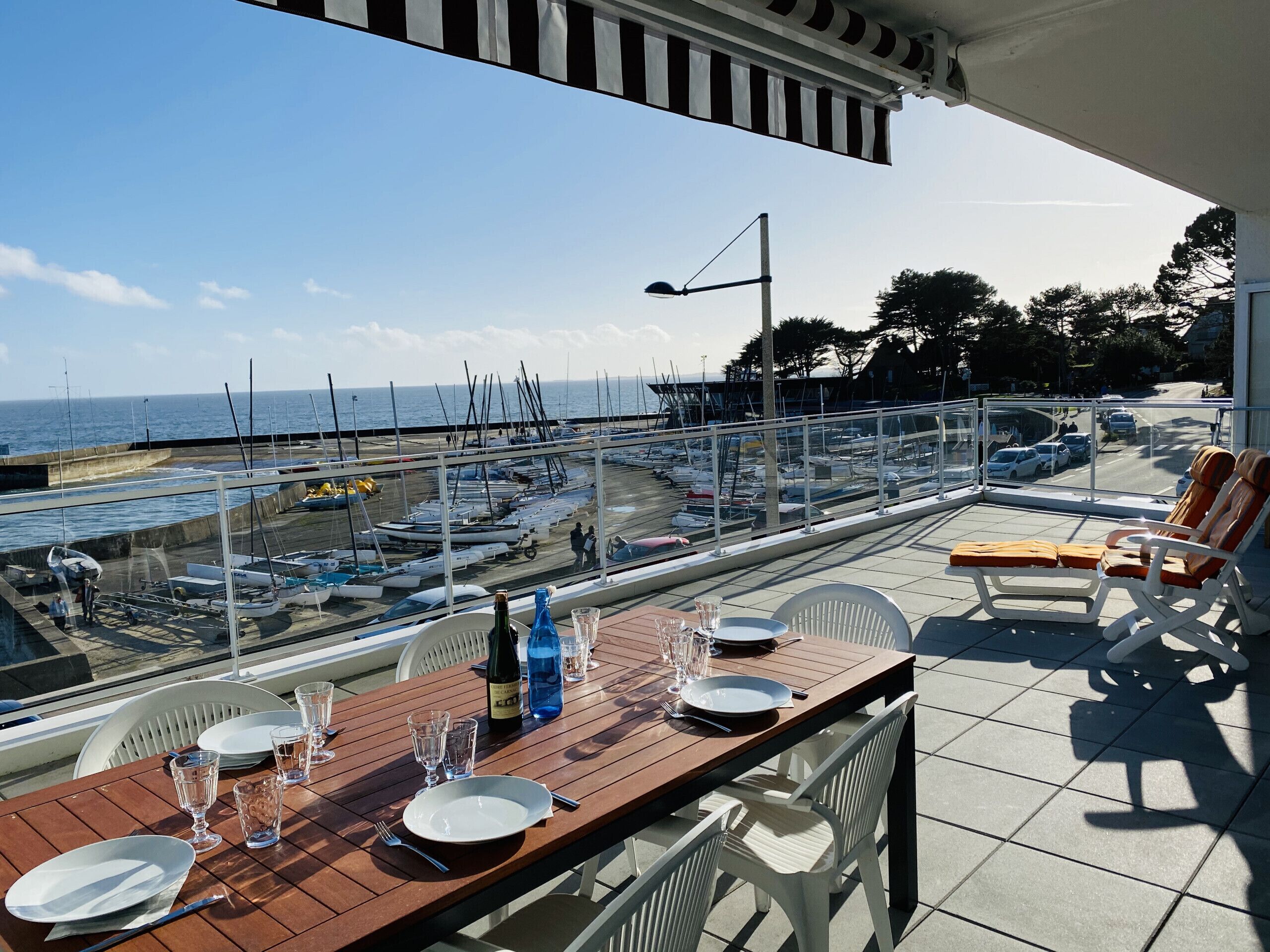 A terrace with a table set for dining, overlooking a marina with boats and a clear sky.