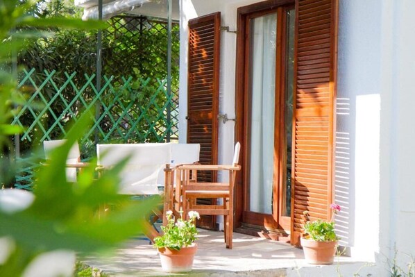 A wooden chair and table outside a building with a green fence and potted plants.