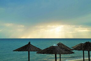 A beach with thatched umbrellas and calm sea.