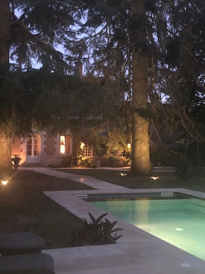 A swimming pool with a clear view of the surrounding area, including a building with illuminated windows and a large tree. - Le Clos Saint Sulpice (Fossé)