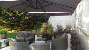An outdoor patio with wicker furniture, a large umbrella, and potted plants. - Le Clos Saint Sulpice (Fossé)