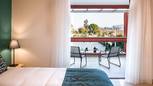 A bedroom with a large bed, a nightstand, a lamp, and a view of a balcony with chairs and a table. - Anemi  Apartments  II (Nafplio)