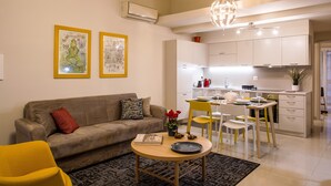 A modern living room with a sofa, a coffee table, and a dining area with chairs and a table. - Anemi  Apartments  II (Nafplio)