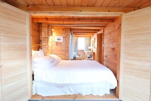Une chambre dans un chalet en bois, avec un lit, une table de chevet et une fenêtre avec des rideaux.