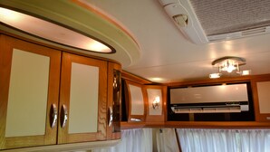 A compact, well-lit interior with wooden cabinets, a built-in air conditioning unit, and a window with curtains. - Big Game on Wheels - Wilpattu (Pahala Maragahawewa)