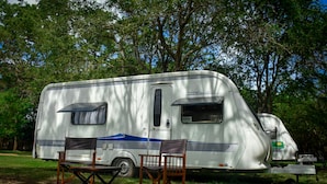 A white RV with a blue stripe and "Prestige" branding parked in a grassy area with trees. - Big Game on Wheels - Wilpattu (Pahala Maragahawewa)