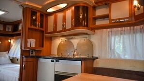 A compact RV kitchen with wooden cabinets, a built-in oven, and a small sink. - Big Game on Wheels - Wilpattu (Pahala Maragahawewa)