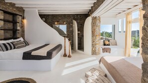 A bedroom with a stone wall, a white ceiling, and a large window. - Villa Princess by Thea-concept (Mykonos)