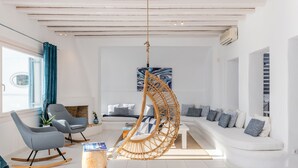 A modern living room with a white sofa, grey rocking chairs, a hanging rattan chair, and a coffee table. - Villa Princess by Thea-concept (Mykonos)