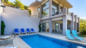 Une maison moderne à deux étages, dotée d’une piscine, de fauteuils de salon bleus et d’un balcon.