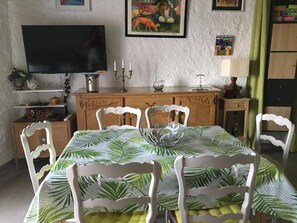 Een eetgedeelte met een tafel voor vier personen, een televisie aan de muur en een kast met decoratieve objecten.