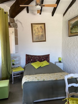 Een slaapkamer met een bed, nachtkastje, kapstok en een schilderij aan de muur.
