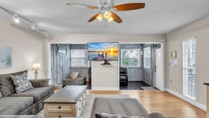 A spacious living room with a ceiling fan, a large TV, and a view of the outdoors through the sliding glass door. - 1 Step Closer 2 Bedroom Villa by RedAwning (Holmes Beach)