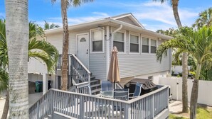 A two-story house with a deck, outdoor furniture, and palm trees. - 1 Step Closer 2 Bedroom Villa by RedAwning (Holmes Beach)
