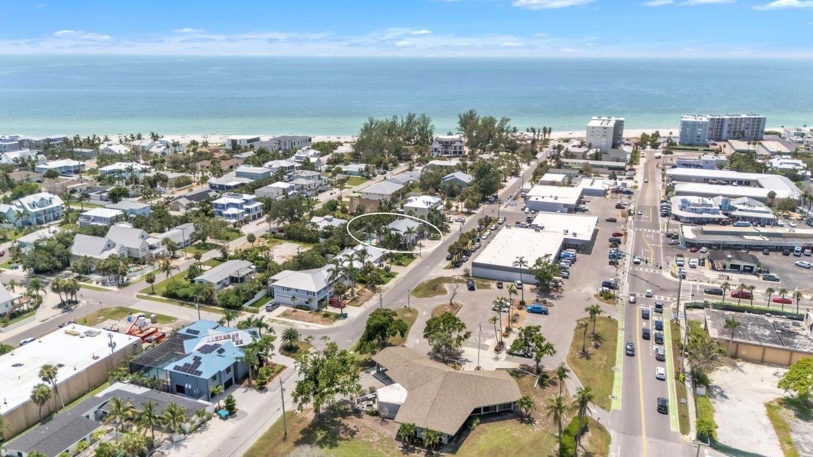 Luftaufnahme einer Küstenstadt mit Wohngebäuden, einer Hauptstraße und einem Strand im Hintergrund.