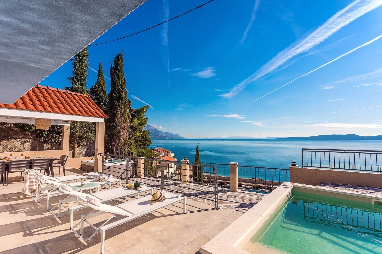 Ein Poolbereich mit Liegestühlen und einem Tisch mit Blick auf ein Gewässer und Berge.