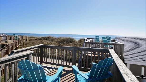A wooden deck with blue Adirondack chairs overlooking the beach. - 19 Oceans Door West Studio Bedroom Condo by RedAwning (Hatteras)