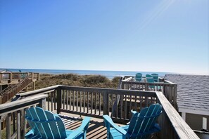 Una terraza de madera con sillas Adirondack azules frente a la playa.