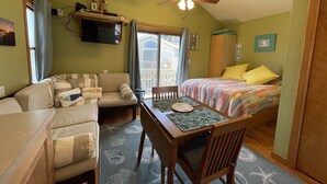A cozy room with a bed, a sofa, a dining table, and a ceiling fan. - 19 Oceans Door West Studio Bedroom Condo by RedAwning (Hatteras)