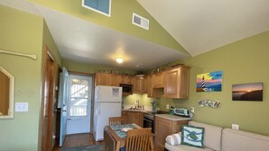 A compact kitchen with wooden cabinets, a refrigerator, microwave, and a dining area with a table and chairs. - 19 Oceans Door West Studio Bedroom Condo by RedAwning (Hatteras)