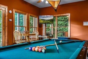 A pool table with balls, a chair, a table with a basket, and a television displaying a landscape. - Ali's Dream 3 Bedroom Cabin by RedAwning (Sevierville)
