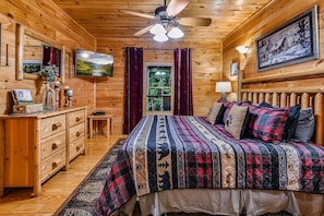 A wooden cabin interior with a bed, a television, a desk, and a window with curtains. - Ali's Dream 3 Bedroom Cabin by RedAwning (Sevierville)