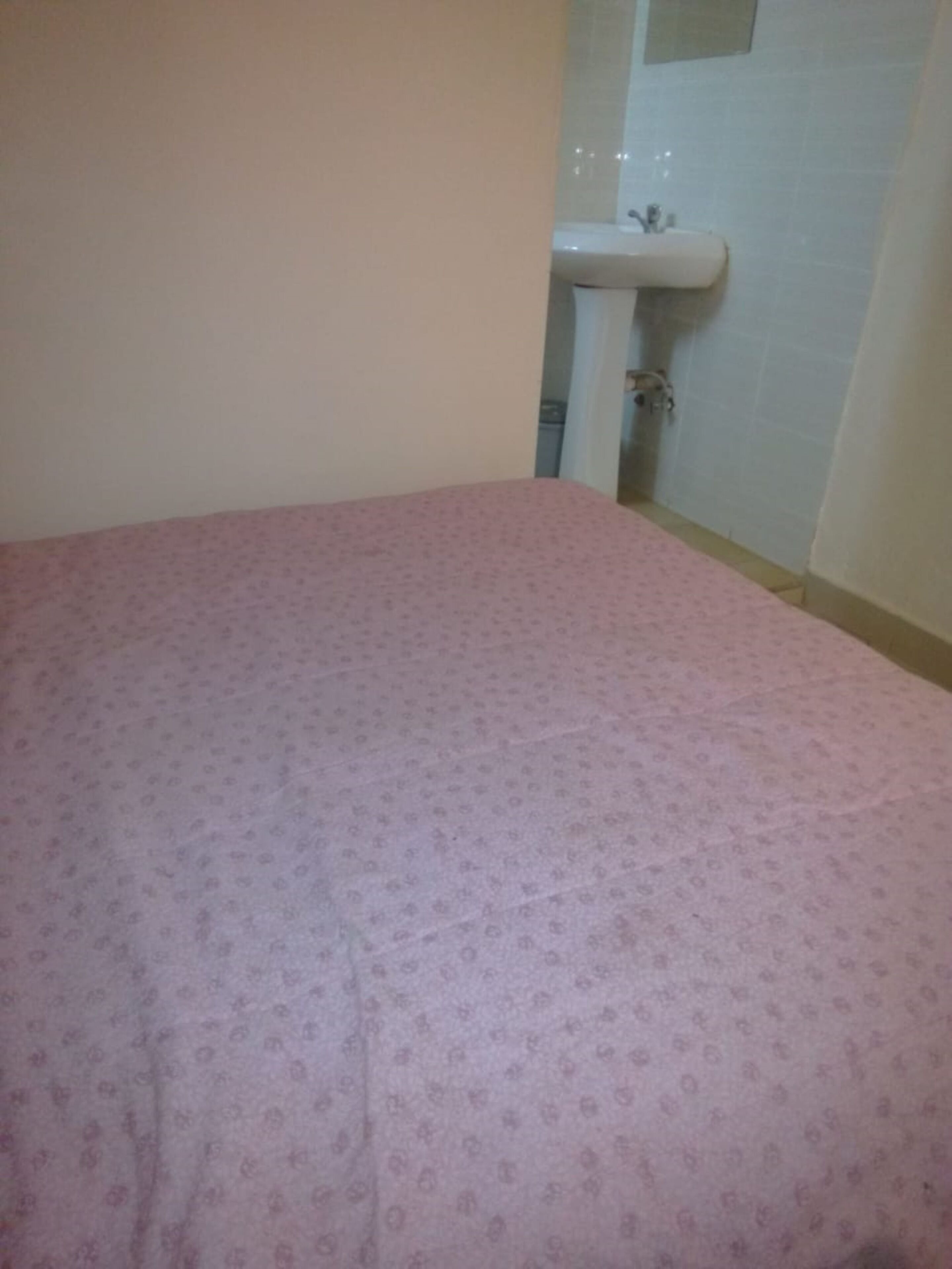 Una habitación con una colcha de cama estampada en tonos rosados, un lavamanos blanco y una pared con azulejos.