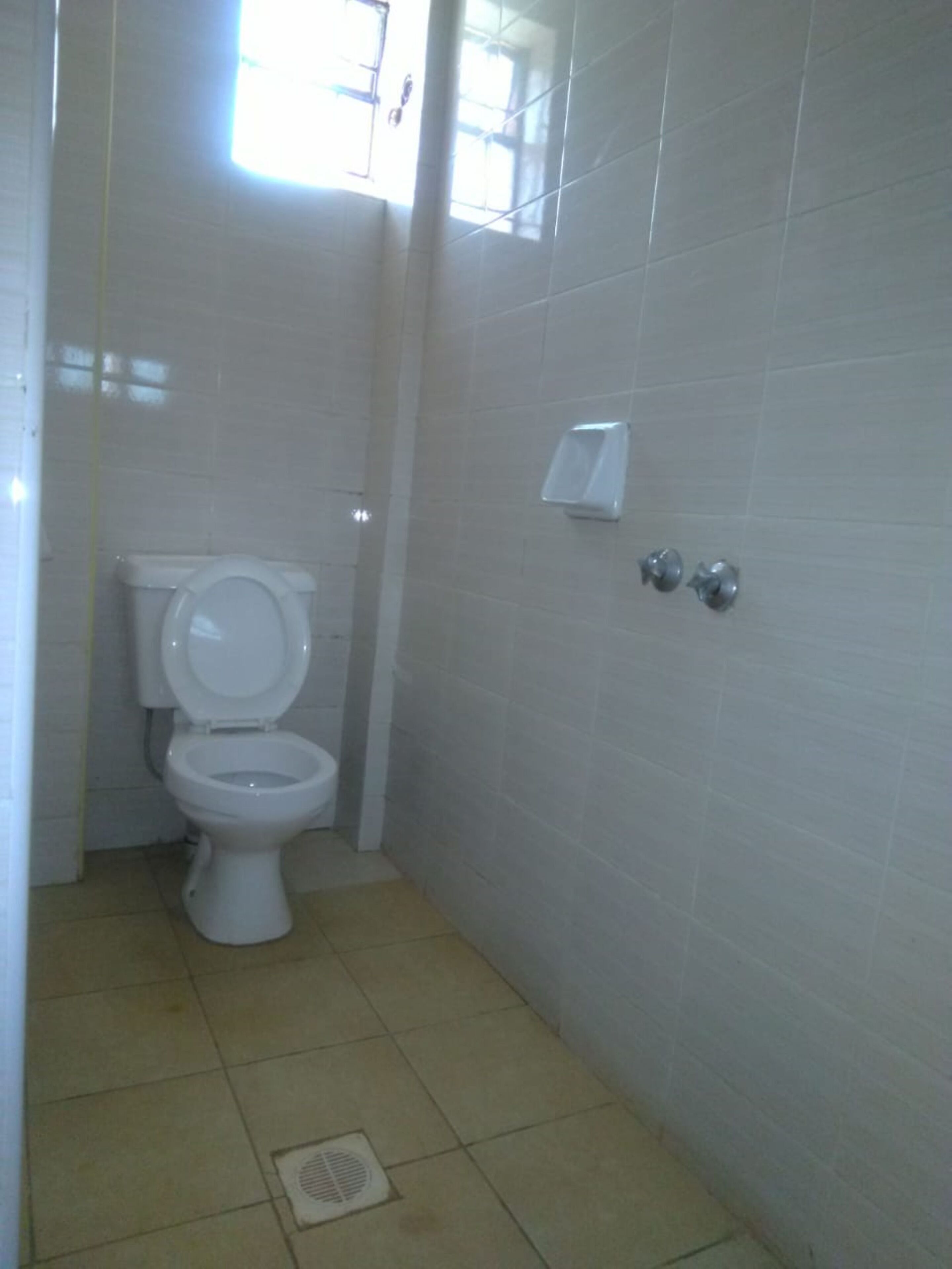 A small, clean bathroom with a toilet, a wall-mounted sink, and a window providing natural light.