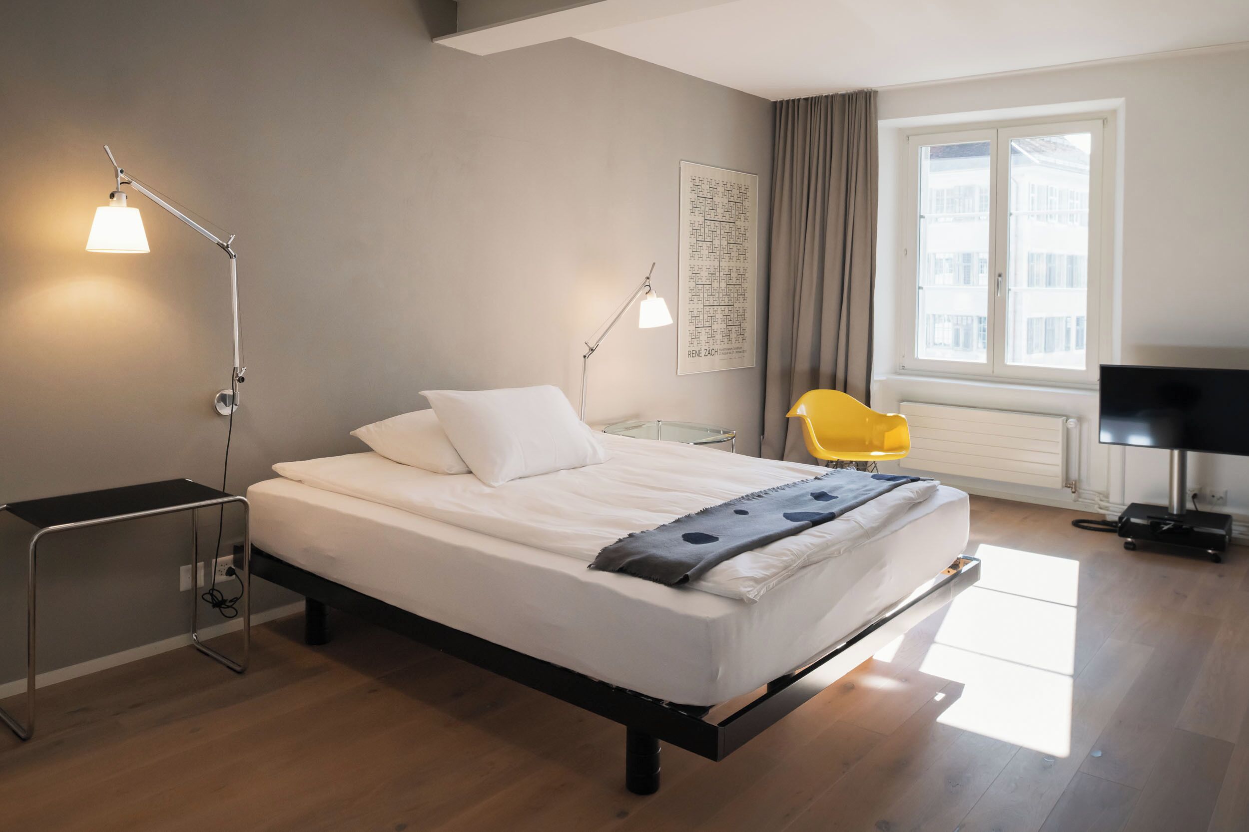 A modern hotel room with a bed, bedside lamps, a window with curtains, and a television.