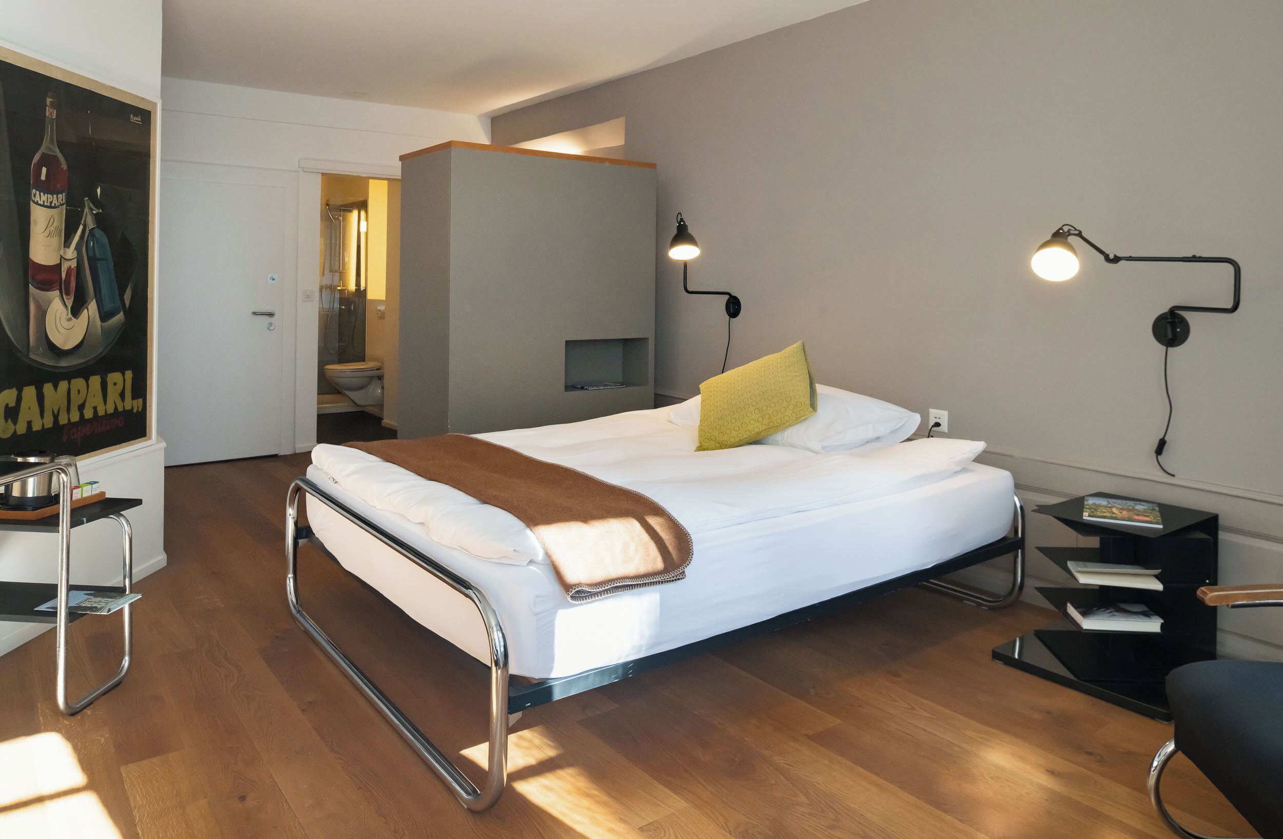 Una habitación de hotel moderna con una cama, mesitas de noche, un escritorio y un baño visible a través de una puerta abierta.