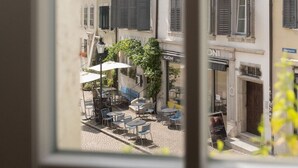 Vista di una strada con tavoli all'aperto, un edificio con persiane e un cartello con scritto 'KUONI'.