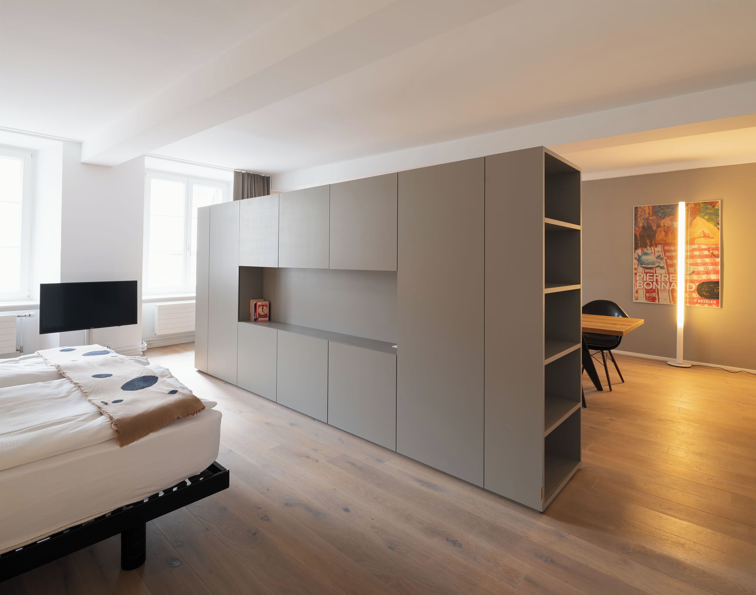 Un dormitorio moderno con cama, televisor, armario y escritorio con silla.