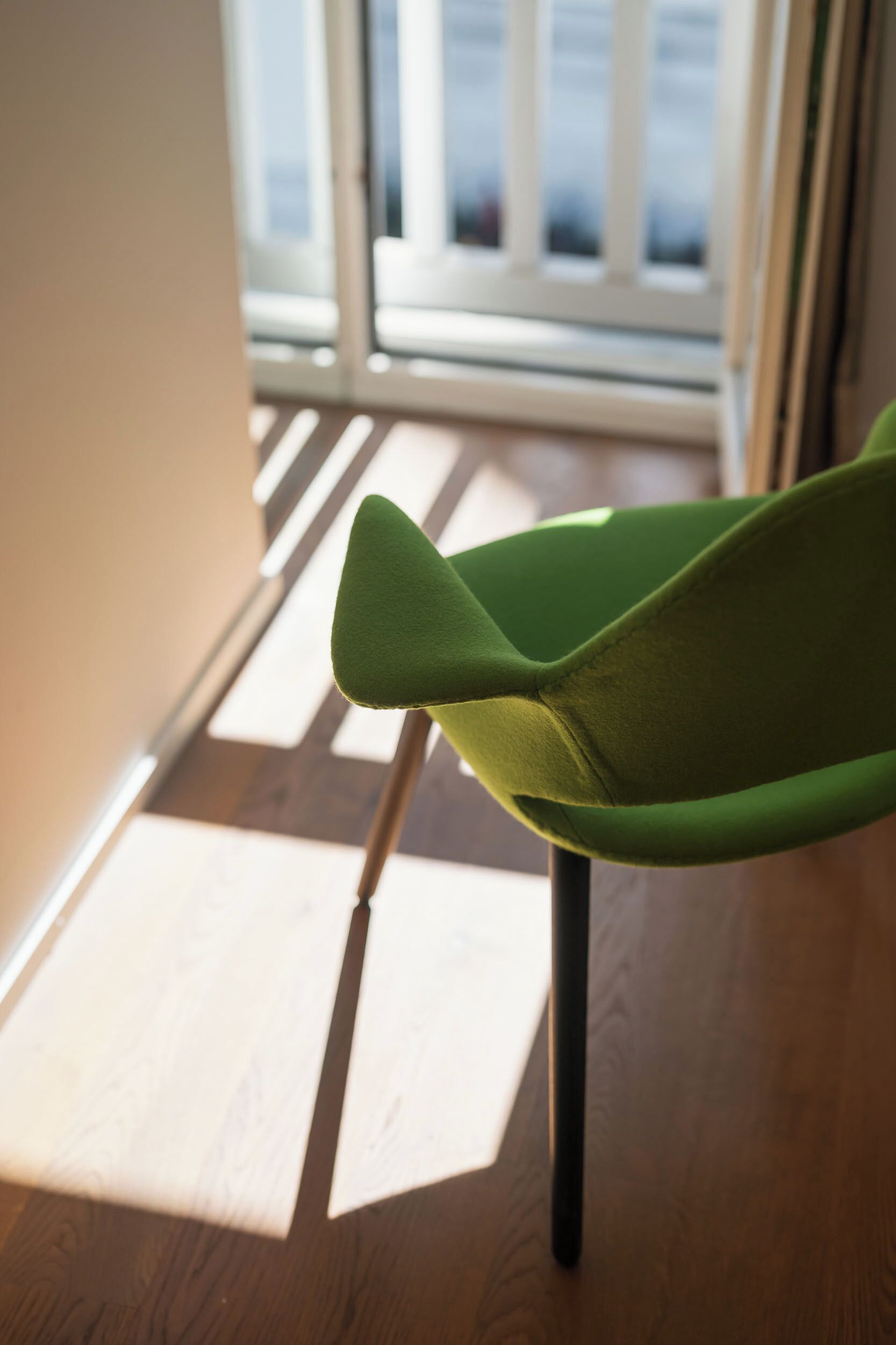 Una silla con respaldo verde y suelo de madera, ubicada cerca de una ventana con persianas.