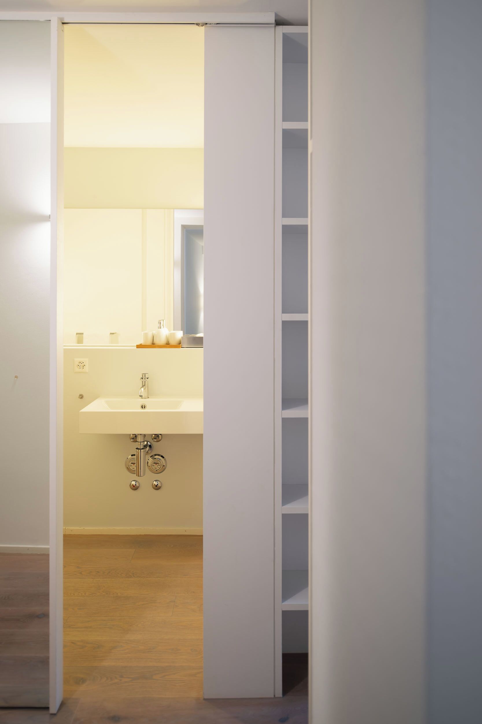 A bathroom with a white sink, mirror, and storage shelves.