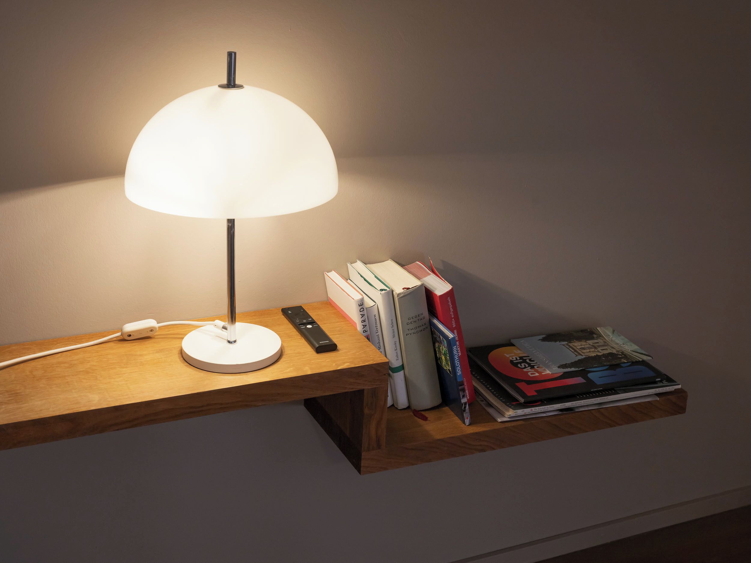 Ein Nachttisch mit Lampe, Fernbedienung und Bücherstapel.
