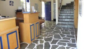 A reception area with a wooden desk, a blue door, and a staircase leading to another floor. - Pension Votsi (Alonissos)
