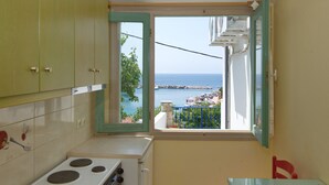 A compact kitchen with a view of the sea, a dining table, and a red chair. - Pension Votsi (Alonissos)