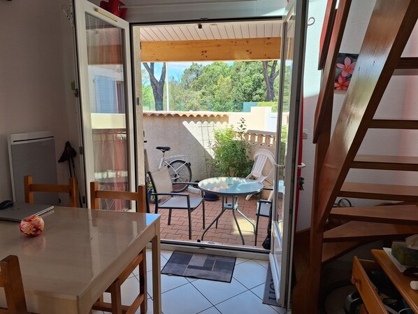An open door leading to a patio with a table and chairs, a bicycle, and a small garden area.