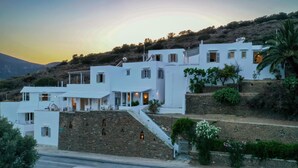 A white building with multiple levels, stone walls, and a staircase leading up to it. - Prasini Gonia (Sifnos)