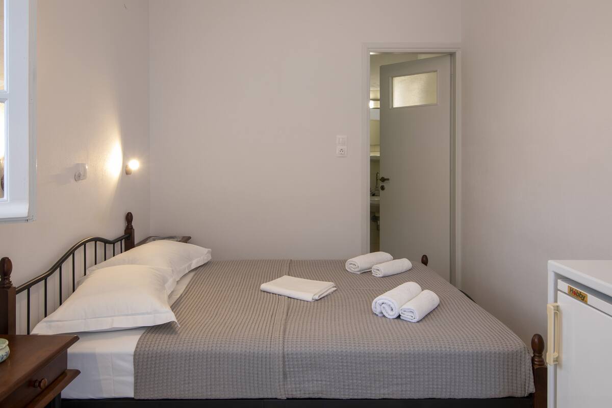 Una cama individual con una colcha gris, dos almohadas y dos toallas enrolladas.