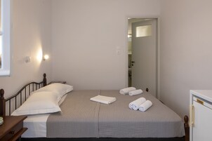 Una cama individual con una colcha gris, dos almohadas y dos toallas enrolladas.