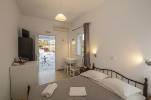 A bedroom with a bed, bedside table, and a desk with a chair. There is a bathroom visible through an open door. - Prasini Gonia (Sifnos)