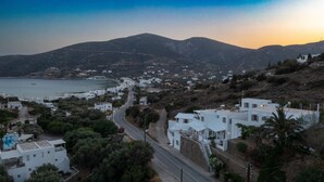 A coastal town with white buildings, a winding road, and a view of the sea and mountains. - Prasini Gonia (Sifnos)