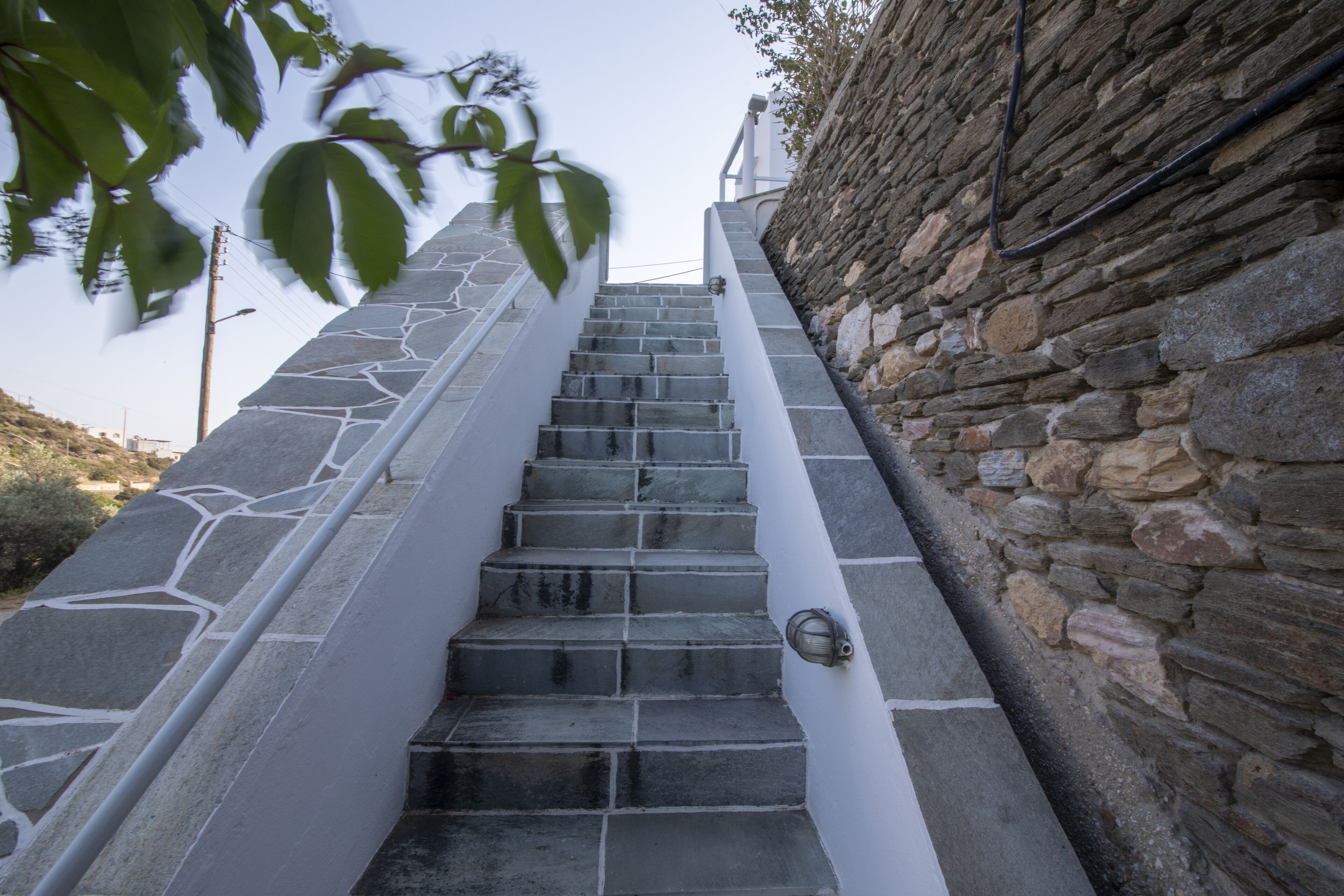 A staircase with stone steps and a white handrail, leading up a stone wall.