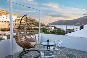 Un balcon avec un fauteuil en osier, une petite table et une vue sur une ville côtière et la mer.