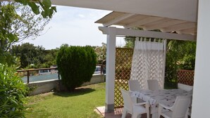 A covered patio with a table and chairs, surrounded by greenery and a pool. - THREE-ROOM APARTMENT BADAS Costa Rei Centro (Costa Rei)